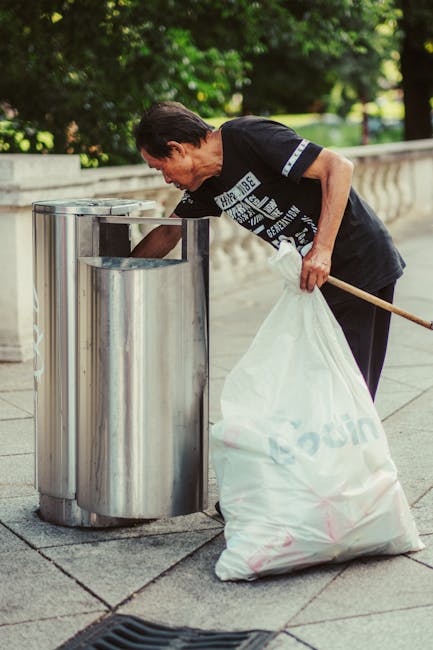 A black plastic wheelie bin with a white label and the words 'ST. JOHN'S' printed on the front, positioned on a residential street sidewalk during nighttime. The bin is open and overflowing with vario